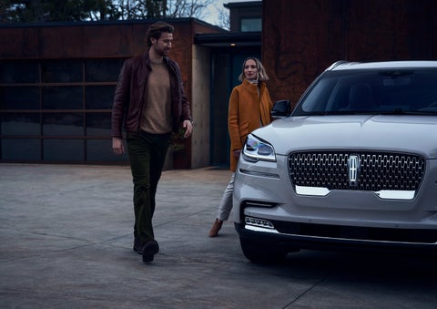 A man and a woman approaching a 2024 Lincoln Aviator® SUV, which illuminates certain lights when they are close | Apple Lincoln Apple Valley in Apple Valley MN