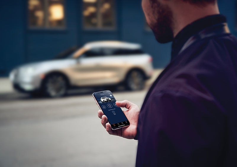 A person is shown interacting with a smartphone to connect to a Lincoln vehicle across the street. | Apple Lincoln Apple Valley in Apple Valley MN