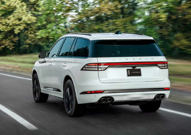 A white 2026 Lincoln Aviator® SUV is being driven away down a road lined with colorful trees. | Apple Lincoln Apple Valley in Apple Valley MN