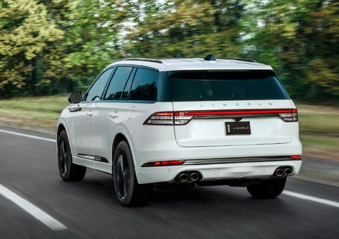 A white 2026 Lincoln Aviator® SUV is being driven away down a road lined with colorful trees. | Apple Lincoln Apple Valley in Apple Valley MN