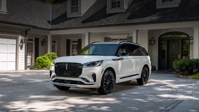 A white 2026 Lincoln Aviator® SUV is parked in the driveway of a luxury home. | Apple Lincoln Apple Valley in Apple Valley MN