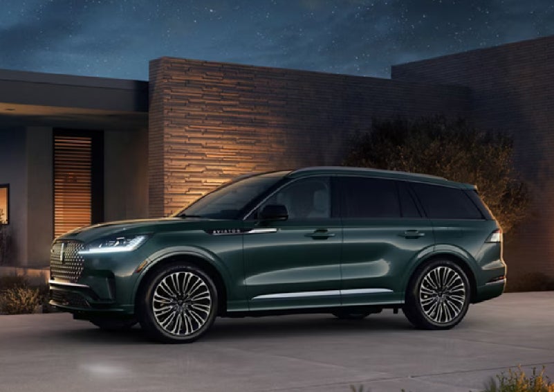 A green 2027 Lincoln Aviator® SUV is parked outside a contemporary home. | Apple Lincoln Apple Valley in Apple Valley MN