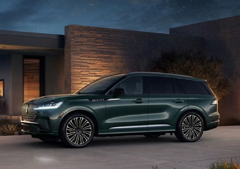 A green 2027 Lincoln Aviator® SUV is parked outside a contemporary home. | Apple Lincoln Apple Valley in Apple Valley MN
