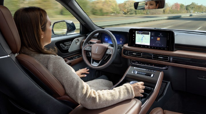 A 2027 Lincoln Aviator® SUV is being driven hands-free on a highway lined with trees. | Apple Lincoln Apple Valley in Apple Valley MN