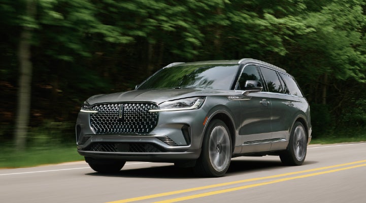 A 2027 Lincoln Aviator® SUV is being driven down a road lined with trees. | Apple Lincoln Apple Valley in Apple Valley MN